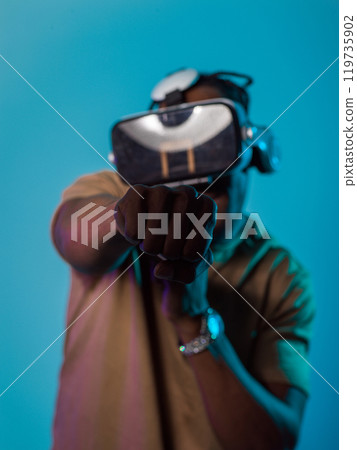 In an avant-garde scene, an African American man engages in cutting-edge virtual reality gaming, utilizing VR glasses to immerse himself in futuristic boxing games, set against a vivid blue background In an avant-garde scene, an African American man engages in cutting-edge virtual reality gaming, utilizing VR glasses to immerse himself in futuristic boxing games, set against a vivid blue background 119735902