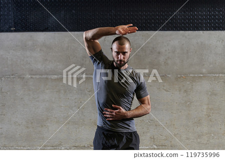 A muscular man working stretching exercises for his arms and body muscles in modern gym A muscular man working stretching exercises for his arms and body muscles in modern gym 119735996