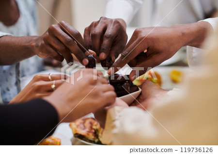 In a poignant close-up, the diverse hands of a Muslim family delicately grasp fresh dates, symbolizing the breaking of the fast during the holy month of Ramadan, capturing a moment of cultural unity 119736126