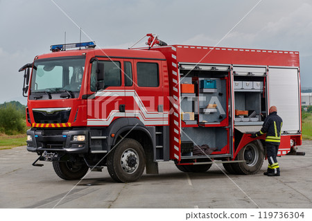 A firefighter meticulously prepares a modern firetruck for a mission to evacuate and respond to dangerous situations, showcasing the utmost dedication to safety and readiness in the face of a fire A firefighter meticulously prepares a modern firetruck for a mission to evacuate and respond to dangerous situations, showcasing the utmost dedication to safety and readiness in the face of a fire 119736304