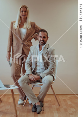 A business couple posing for a photograph together against a beige backdrop, capturing their professional partnership and creating a timeless image of unity and success. A business couple posing for a photograph together against a beige backdrop, capturing their professional partnership and creating a timeless image of unity and success. 119736374