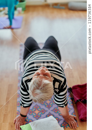 Senior Woman Practicing Back Stretches in a Sunlit Space for Optimal Health and Well Being 119736384
