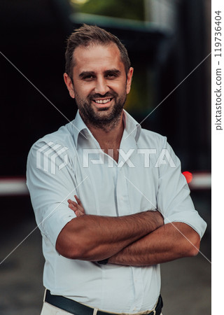 A successful businessman in a white shirt with crossed arms posing outdoors A successful businessman in a white shirt with crossed arms posing outdoors 119736404