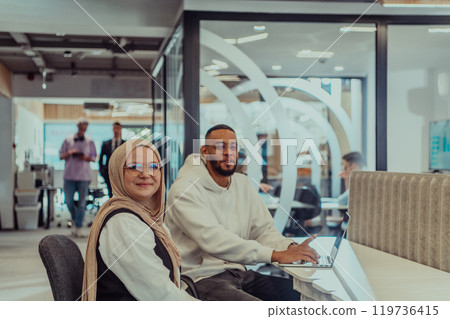 In a modern office setting, an African American businessman and his Muslim colleague, wearing a hijab, engage in collaborative discussions, tackling various business tasks and solving problems 119736415