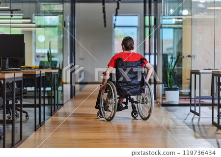 A modern young businesswoman in a wheelchair is surrounded by an inclusive workspace with glass-walled offices, embodying determination and innovation in the business world 119736434