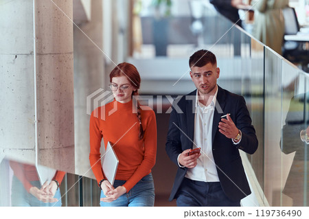 In the dynamic environment of a modern startup company, the director engages in a discussion with his young business colleague while they walk, reflecting the spirit of collaboration and innovation in 119736490