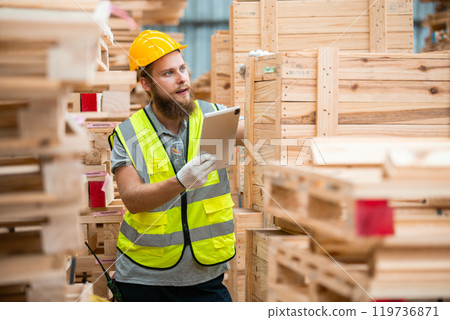 Worker Man with a bearded wearing safety uniform hard hat holding tablet working checking quality wooden at manufacturing wooden. Male carpenter worker wood warehouse industry. Worker Man with a bearded wearing safety uniform hard hat holding tablet working checking quality wooden at manufacturing wooden. Male carpenter worker wood warehouse industry. 119736871