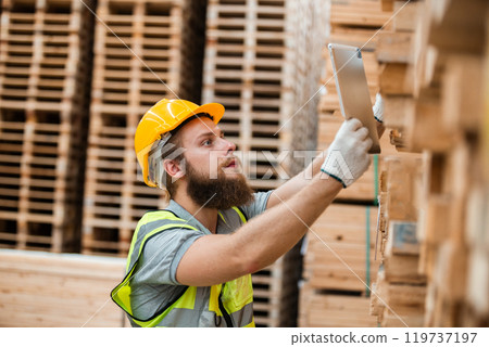 Worker Man with a bearded wearing safety uniform hard hat holding tablet working checking quality wooden at manufacturing wooden. Male carpenter worker wood warehouse industry. 119737197