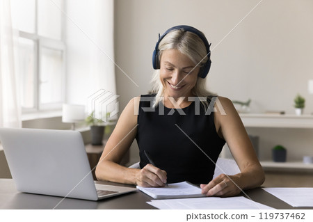 Diligent mature female in earphones engaged in e-learning on laptop 119737462