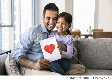 Happy Indian dad holding greeting card and daughter in arms Happy Indian dad holding greeting card and daughter in arms 119737473