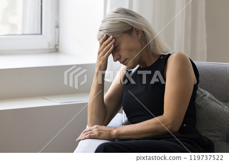 Stressed nervous aged female sit on couch with eyes closed 119737522