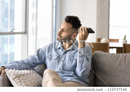 Serious young Latin man listening to voice message on phone Serious young Latin man listening to voice message on phone 119737548