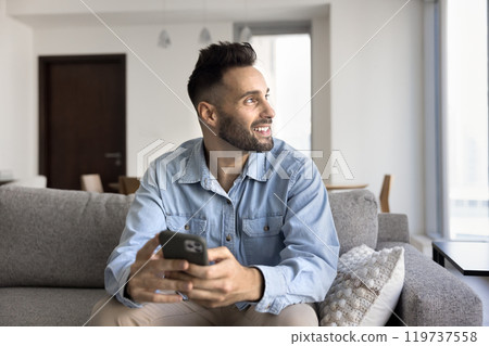 Dreamy positive handsome Latin man using gadget for online communication 119737558