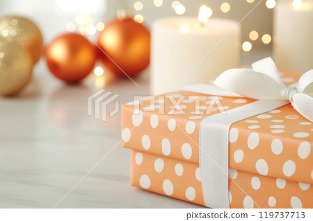 A beautifully wrapped orange gift box with white polka dots sits on a festive table 119737713