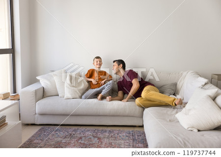 Joyful son child and happy Latin daddy resting on sofa Joyful son child and happy Latin daddy resting on sofa 119737744