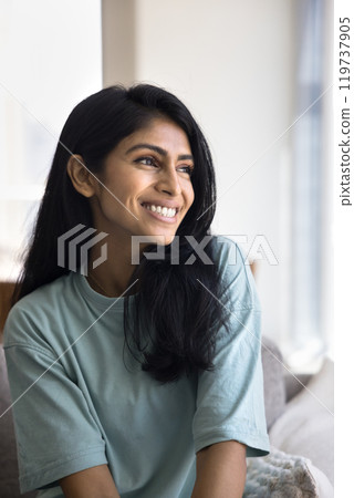 Positive attractive young 20s Indian woman sitting on home sofa 119737905