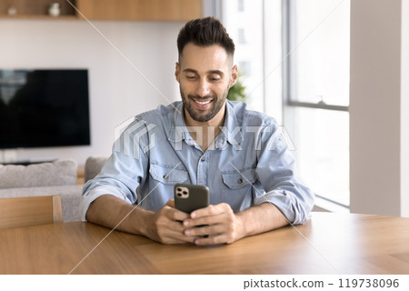 Positive Hispanic man typing on mobile phone at home workplace Positive Hispanic man typing on mobile phone at home workplace 119738096