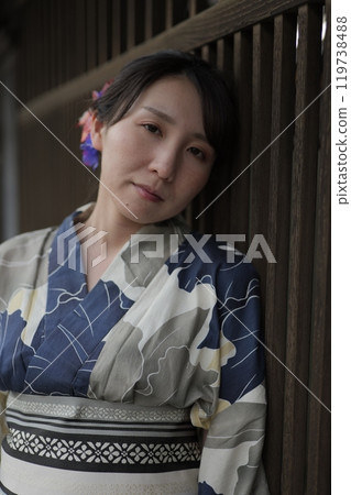 A young woman in a yukata standing at a lattice door 119738488