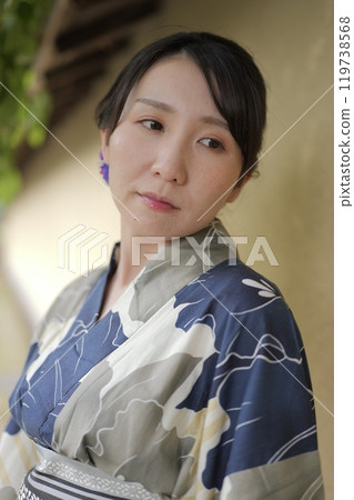 A young woman in a yukata standing against a wall 119738568