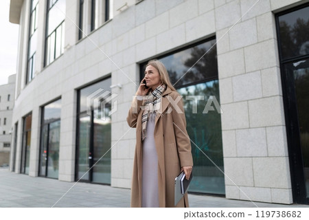 A businesswoman walks outside of a business center, talking on her phone A businesswoman walks outside of a business center, talking on her phone 119738682