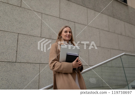 A businesswoman walks up stairs near a business center, carrying a laptop and a notebook 119738697