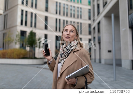 A businesswoman checks her phone while walking outside a business center 119738793