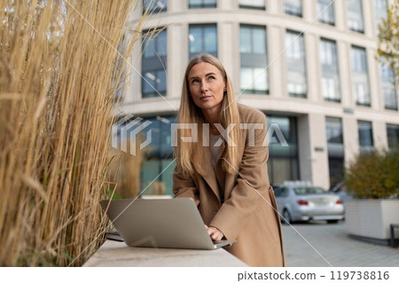 A businesswoman is working on her laptop outside a modern office building A businesswoman is working on her laptop outside a modern office building 119738816