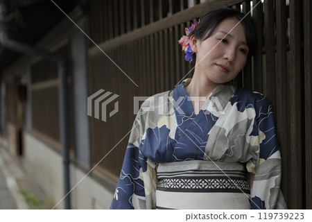 A young woman in a yukata standing at a lattice door 119739223