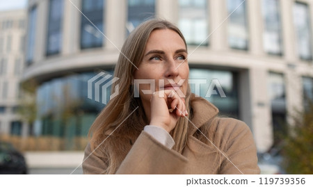 A business woman stands near a modern office building, thinking about her day ahead 119739356