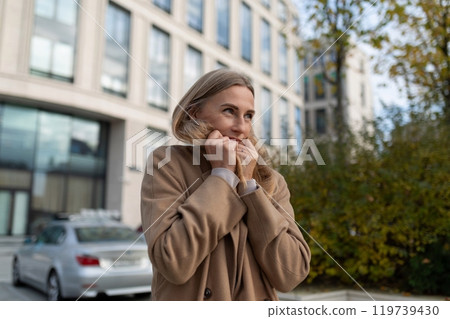 A businesswoman stands near a business center, shivering in the cold 119739430