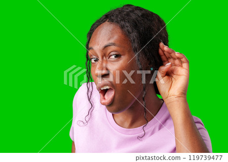 Young woman playfully listening with a smile against a vibrant green background 119739477