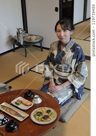 昭和時代的餐點:一位穿著浴衣的年輕女子坐在圓桌旁 昭和時代的餐點:一位穿著浴衣的年輕女子坐在圓桌旁 119739489