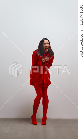Woman dressed in vibrant red suit laughing with sense of unrestrained joy, embodying confidence and vitality. 119741030