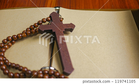Dark red wooden cross leaning against an old open book symbolizing the spread of Jesus Christs love among Christians reflecting faith devotion and the importance of Christian teachings. 119741105