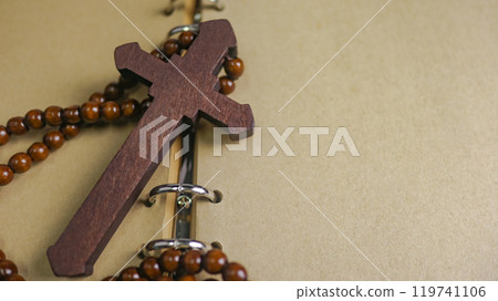 Dark red wooden cross leaning against an old open book symbolizing the spread of Jesus Christs love among Christians reflecting faith devotion and the importance of Christian teachings. 119741106