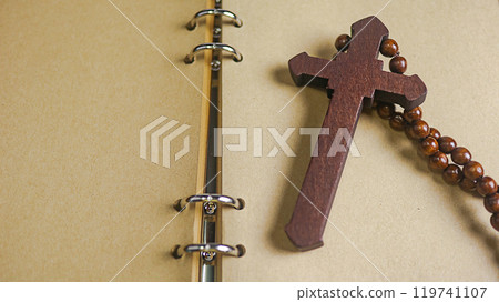 Dark red wooden cross leaning against an old open book symbolizing the spread of Jesus Christs love among Christians reflecting faith devotion and the importance of Christian teachings. 119741107