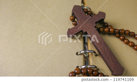 Dark red wooden cross leaning against an old open book symbolizing the spread of Jesus Christs love among Christians reflecting faith devotion and the importance of Christian teachings. Dark red wooden cross leaning against an old open book symbolizing the spread of Jesus Christs love among Christians reflecting faith devotion and the importance of Christian teachings. 119741109