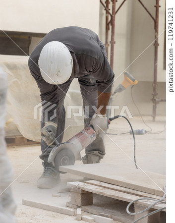 Craftsman in grey work clothes and helmet cutting marble piece during construction 119741231