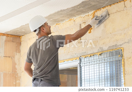 Craftsmen in grey clothes working inside a room standing on scaffoldings during construction 119741233
