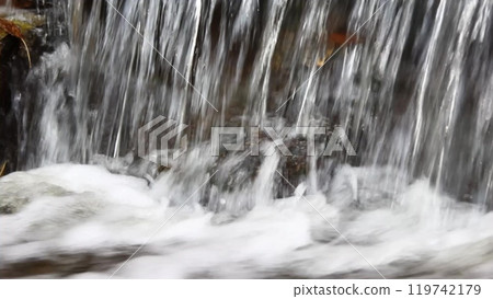 Waterfall cascading down rocky terrain, with yellow leaves drifting on the water and foam forming at the base. A calm, seasonal moment in the heart of nature. Waterfall cascading down rocky terrain, with yellow leaves drifting on the water and foam forming at the base. A calm, seasonal moment in the heart of nature. 119742179