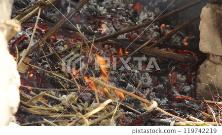 Watch as dry herbs are carefully placed in a street stove made of white bricks, igniting a fragrant smoke. The process highlights the traditional method of herb burning in an outdoor setting. 119742219