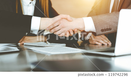 Unknown businessman shaking hands with his colleague or partner above the desk in sunny office, close-up 119742296