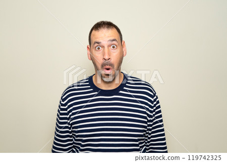 Hispanic man with beard about 40s scared and shocked with surprise expression, fear and excited face. Isolated on beige background. 119742325