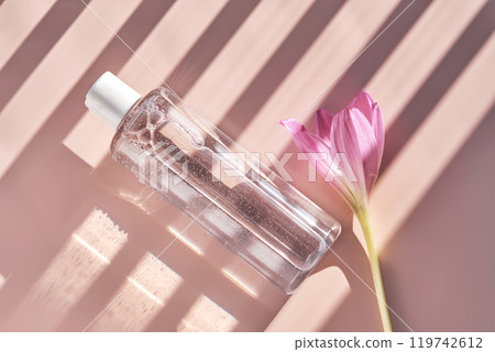 Bottle of facial toner or cleanser on a pink background with stripes shadows. 119742612
