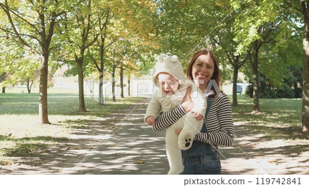 A joyful and heartwarming moment of a mother gently holding her baby in a beautiful park surrounded by lush trees 119742841