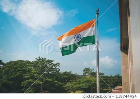 Indian flag waving on a flagpole in front of green trees and blue sky 119744454