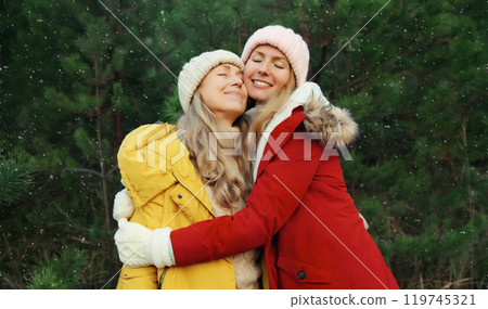 Happy smiling mature mother and adult daughter hugs in winter forest, Christmas tree with snow 119745321