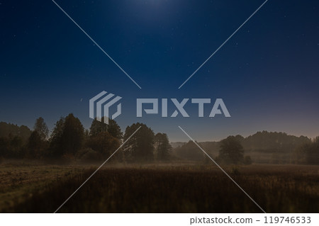 A serene night scene of a starry sky over misty fields and a dark forest. The moonlight illuminates the tranquil landscape, creating a peaceful atmosphere perfect for nature and night photography love 119746533