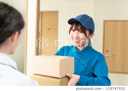 A young woman in work clothes receiving a parcel and a female courier A young woman in work clothes receiving a parcel and a female courier 119747352