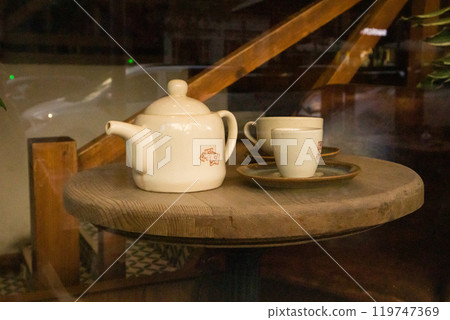 Brown kitchen mock up design. Tableware set. Ceramic beige teapot and two cups stand on a wooden round table in cafe, restaurant Dark key food and drink photo. Morning breakfast. Traditional tea party Brown kitchen mock up design. Tableware set. Ceramic beige teapot and two cups stand on a wooden round table in cafe, restaurant Dark key food and drink photo. Morning breakfast. Traditional tea party 119747369